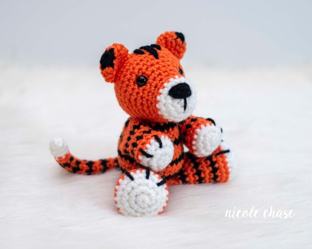 Amigurumi tiger made with this free tiger crochet pattern. The tiger has white on the tip of the tail, snout, and bottom of the hands and feet, and is orange with black stripes.
