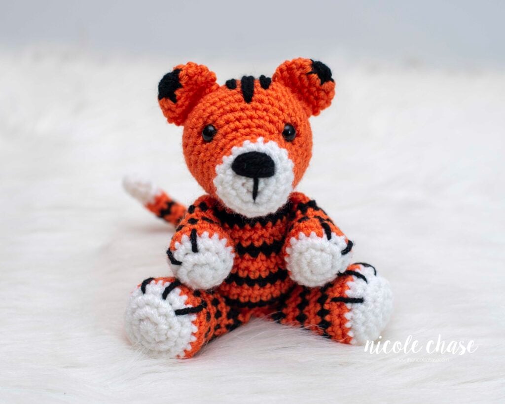 finished crochet tiger made with this free tiger crochet pattern in a bright orange yarn with black stripes and white details