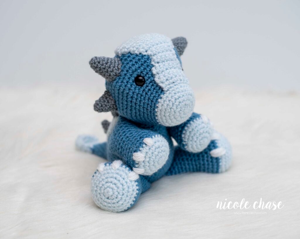 Finished crochet dino made with the free ankylosaurus crochet pattern in the colors blue, light blue, and gray