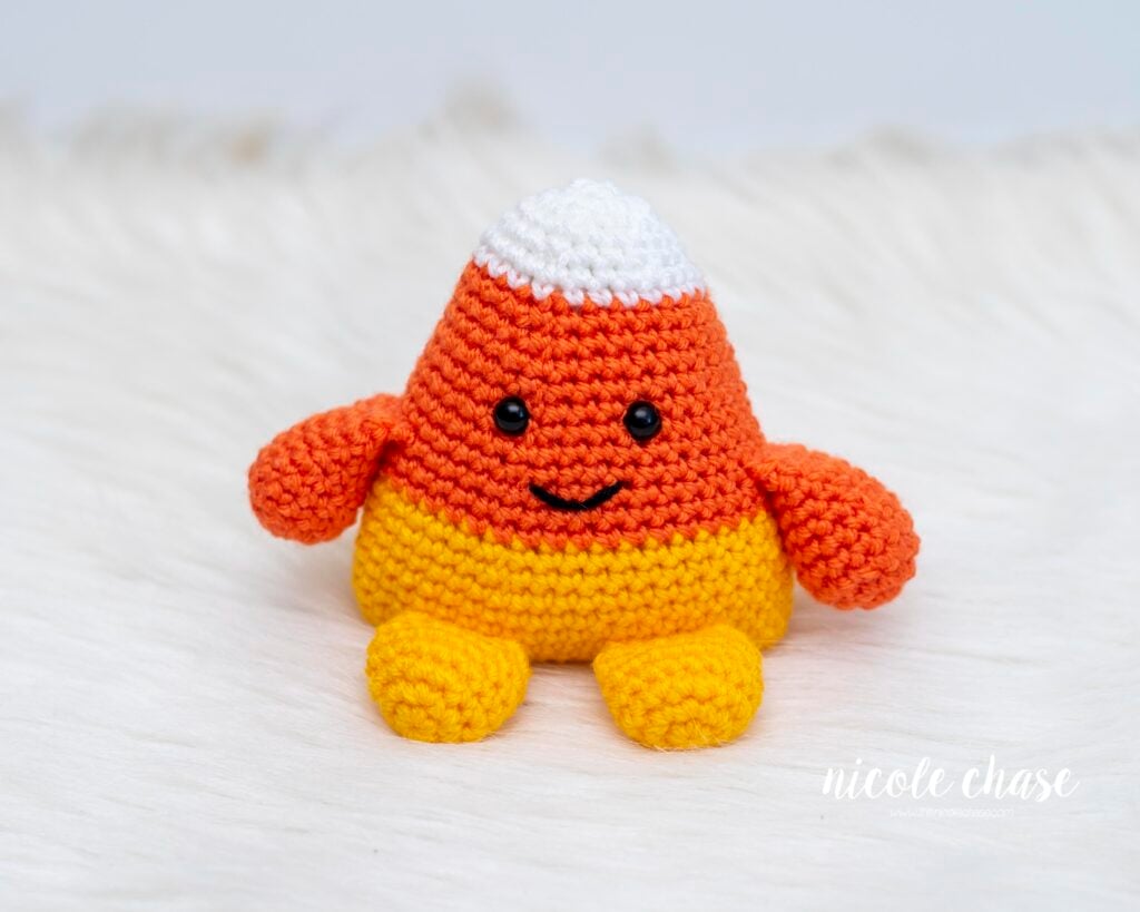 Free candy corn crochet pattern shown sitting on white fur with a white background