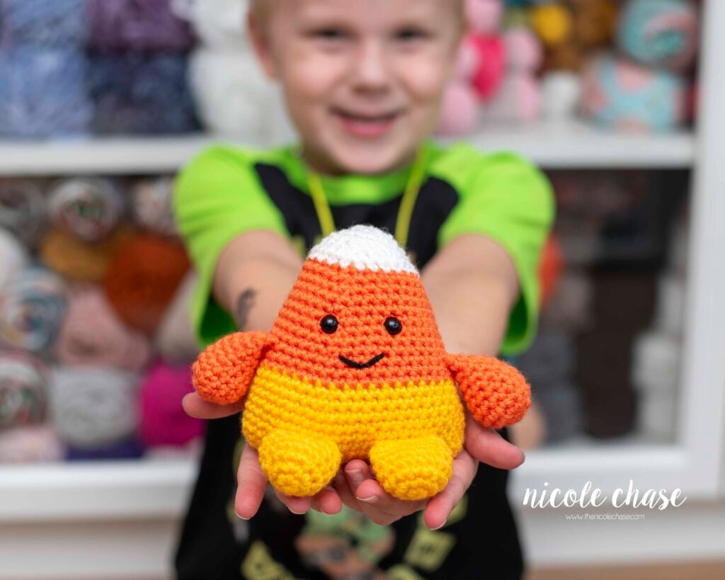 A smiling little boy holding the amigurumi out in front of him made with this free candy corn crochet pattern
