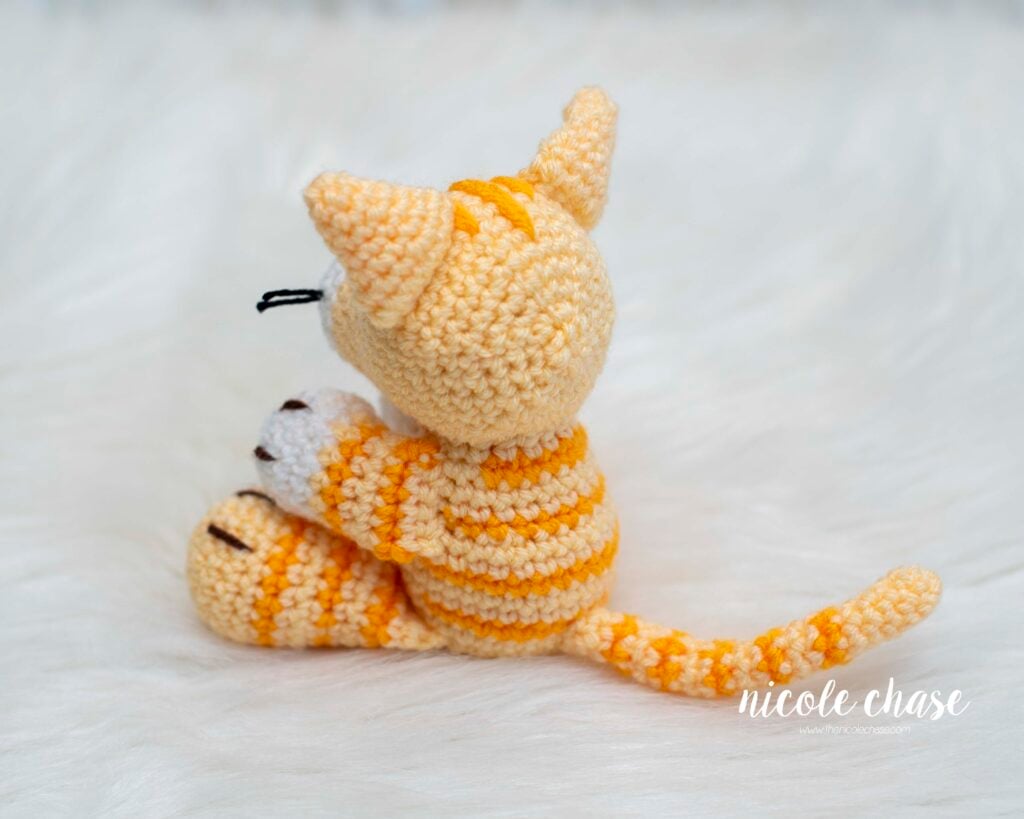 A back view of the finished crochet at, showing the details of the stripes on its body, tail, arm, and leg. 
