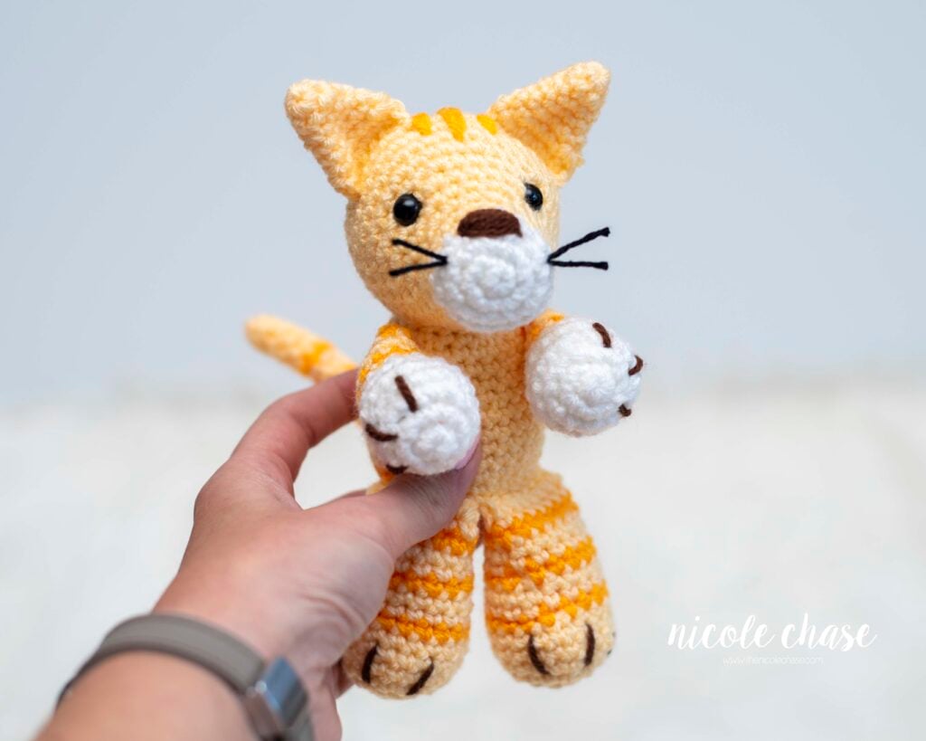 An orange and white tabby cat being held in a hand, named Cooper, a free cat crochet pattern. 