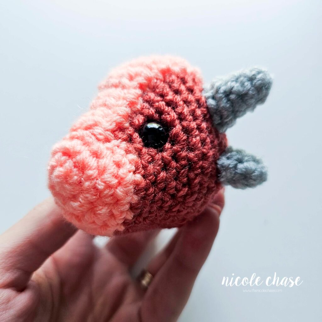 Small spikes of the small dinosaur crochet patterns free sewn into place on the head of Mini Archie, view 1.
