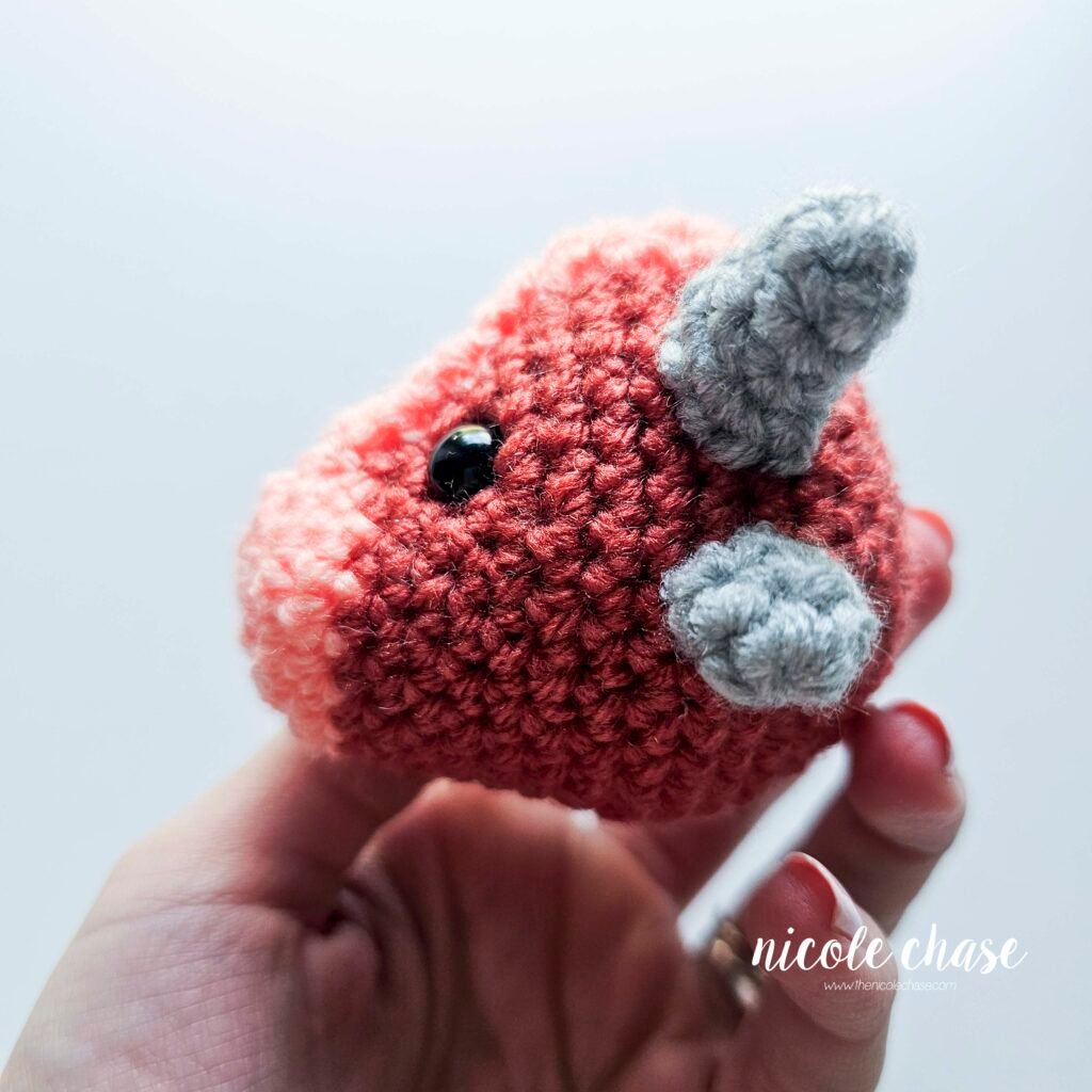 Small spikes of the small dinosaur crochet patterns free sewn into place on the head of Mini Archie, view 2.
