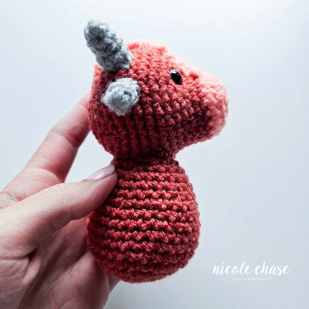 Small ankylosaurus head sewn onto the body of the dinosaur amigurumi, view 1.