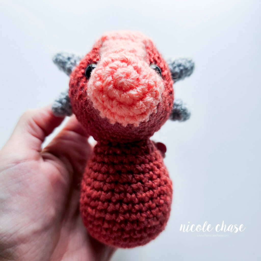 Small ankylosaurus head sewn onto the body of the dinosaur amigurumi, view 2.