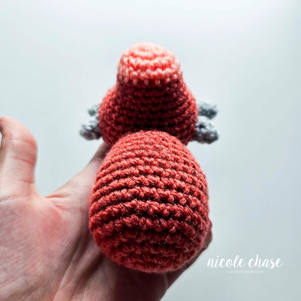 Small ankylosaurus head sewn onto the body of the dinosaur amigurumi, view 3.