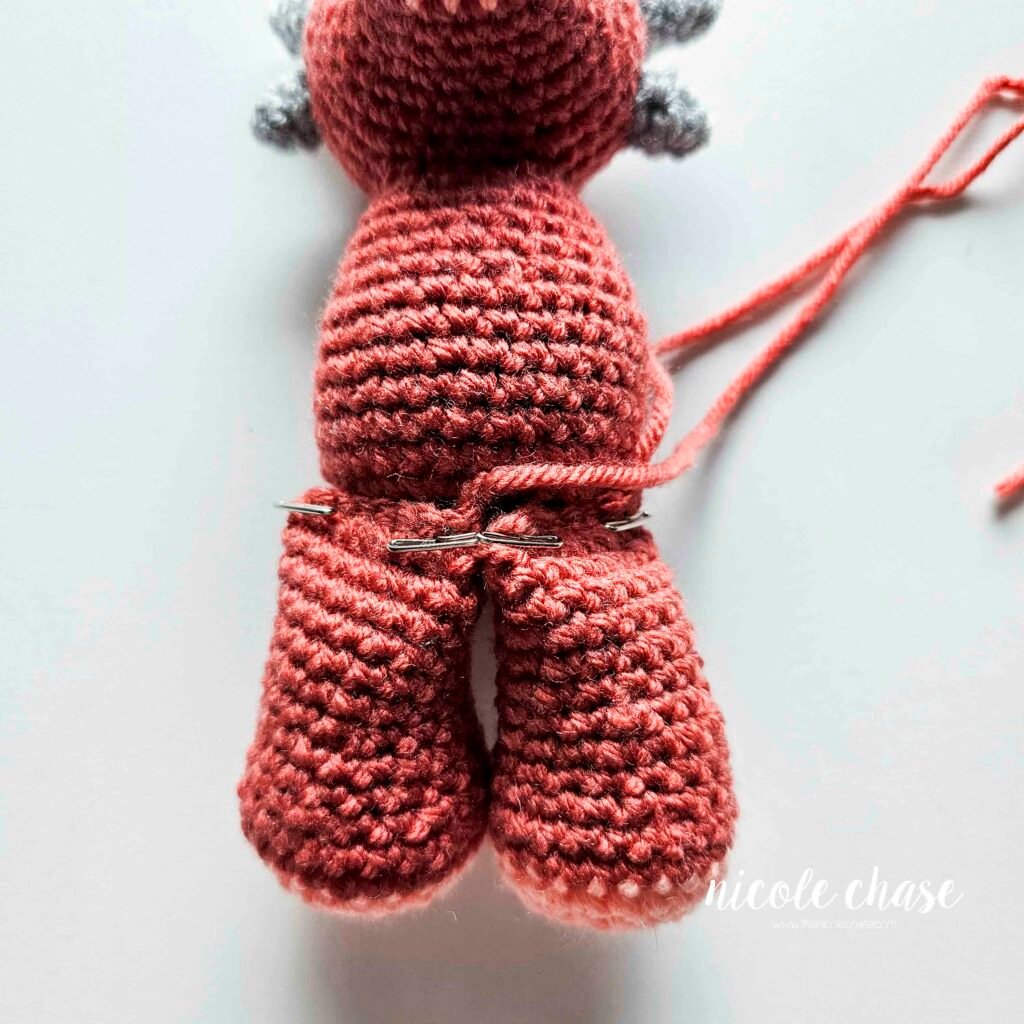 Legs of the ankylosaurus crochet pattern pinned into place on the body before sewing.
