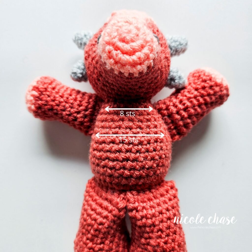 Crochet arms of the ankylosaurus amigurumi sewn into place on the body, view 1.
