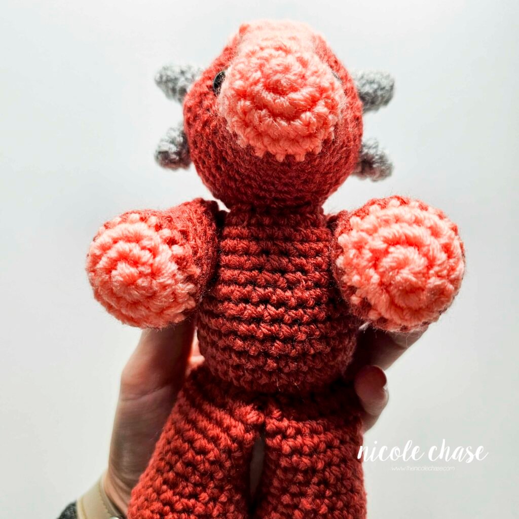Crochet arms of the ankylosaurus amigurumi sewn into place on the body, view 2.