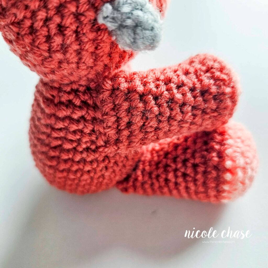 Crochet arms of the ankylosaurus amigurumi sewn into place on the body, view 3.