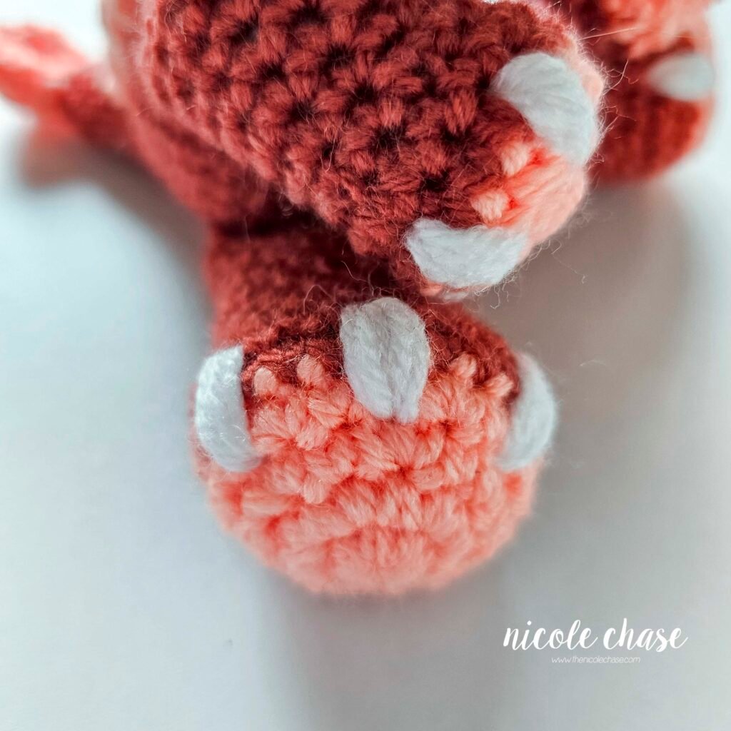 White nails embroidered on the crochet leg of the ankylosaurus amigurumi.