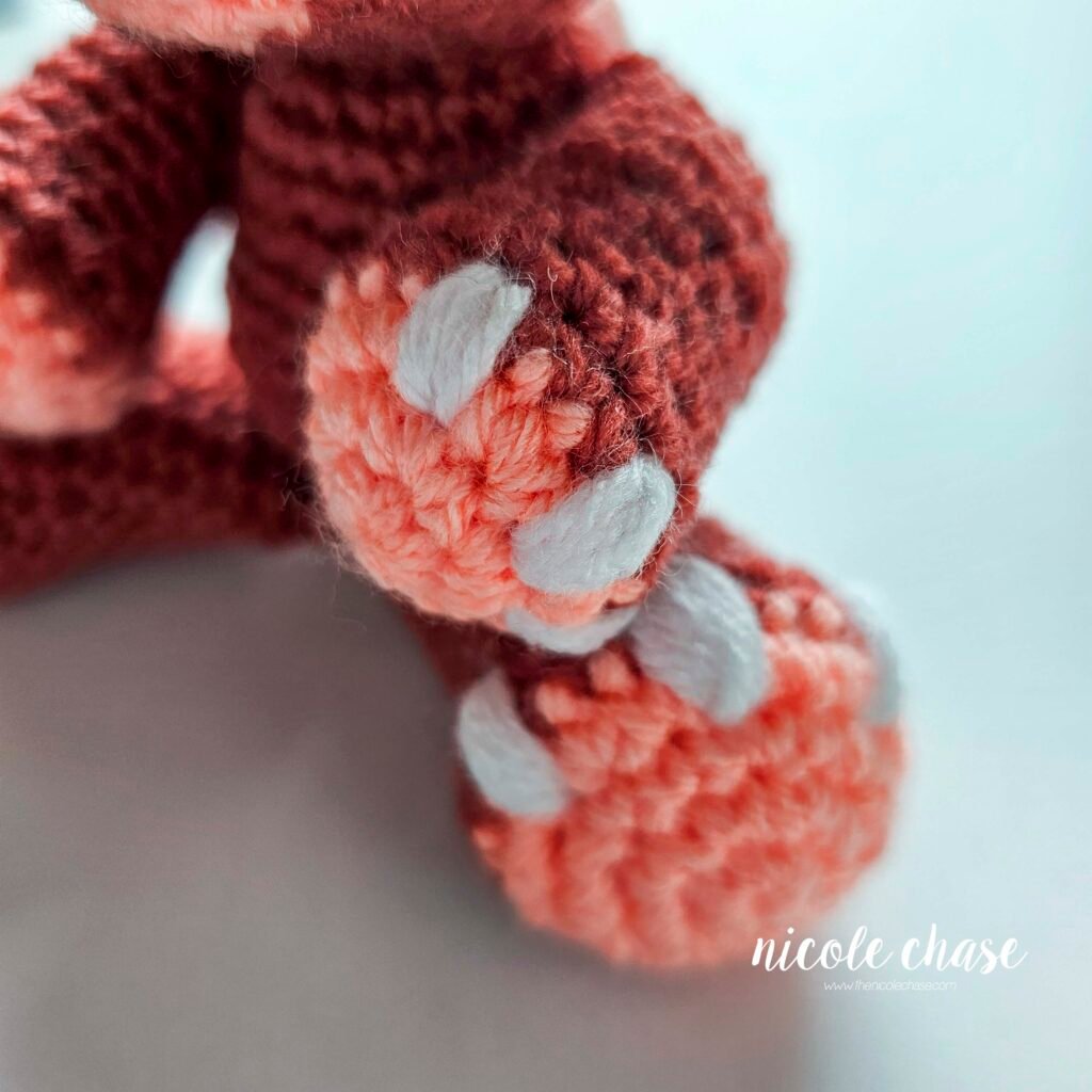 White nails embroidered on the crochet arm of the ankylosaurus amigurumi.