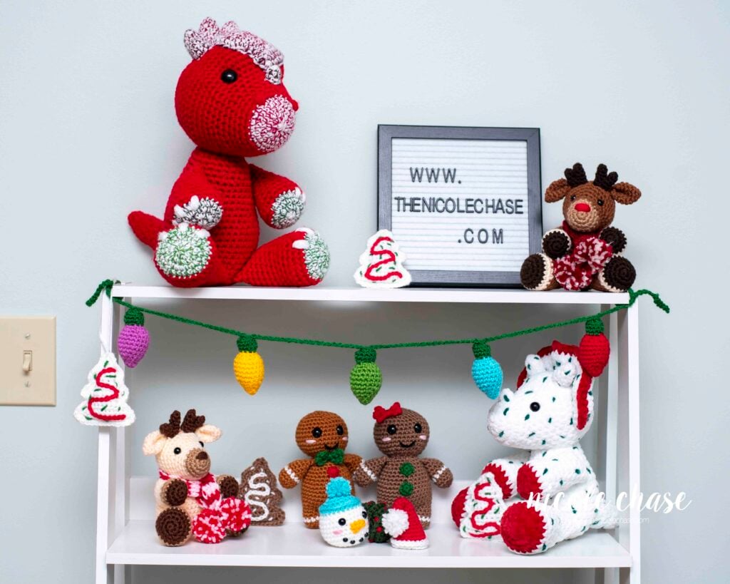 Holiday shelf display featuring the crochet Christmas lights garland strung across the top, alongside several finished crochet animal amigurumi for holiday decoration ideas. 