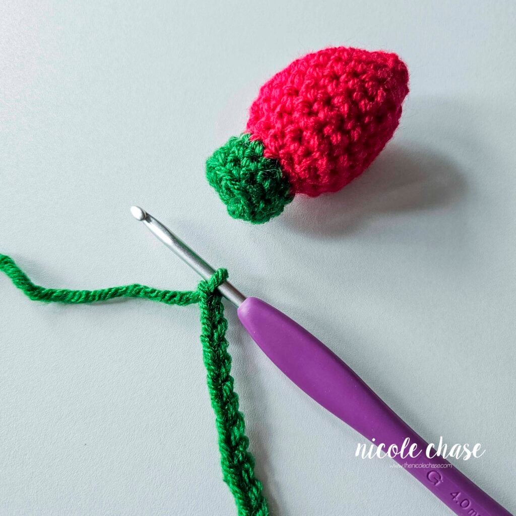 Connecting the green chain to the top of the first crochet holiday light, step 1.