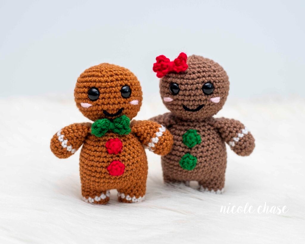 Two finished Gerry the Gingerbread amigurumi: one with a green bow tie and one with a red hair bow, demonstrating customization options. Get the nearly no-sew crochet gingerbread man free pattern. 