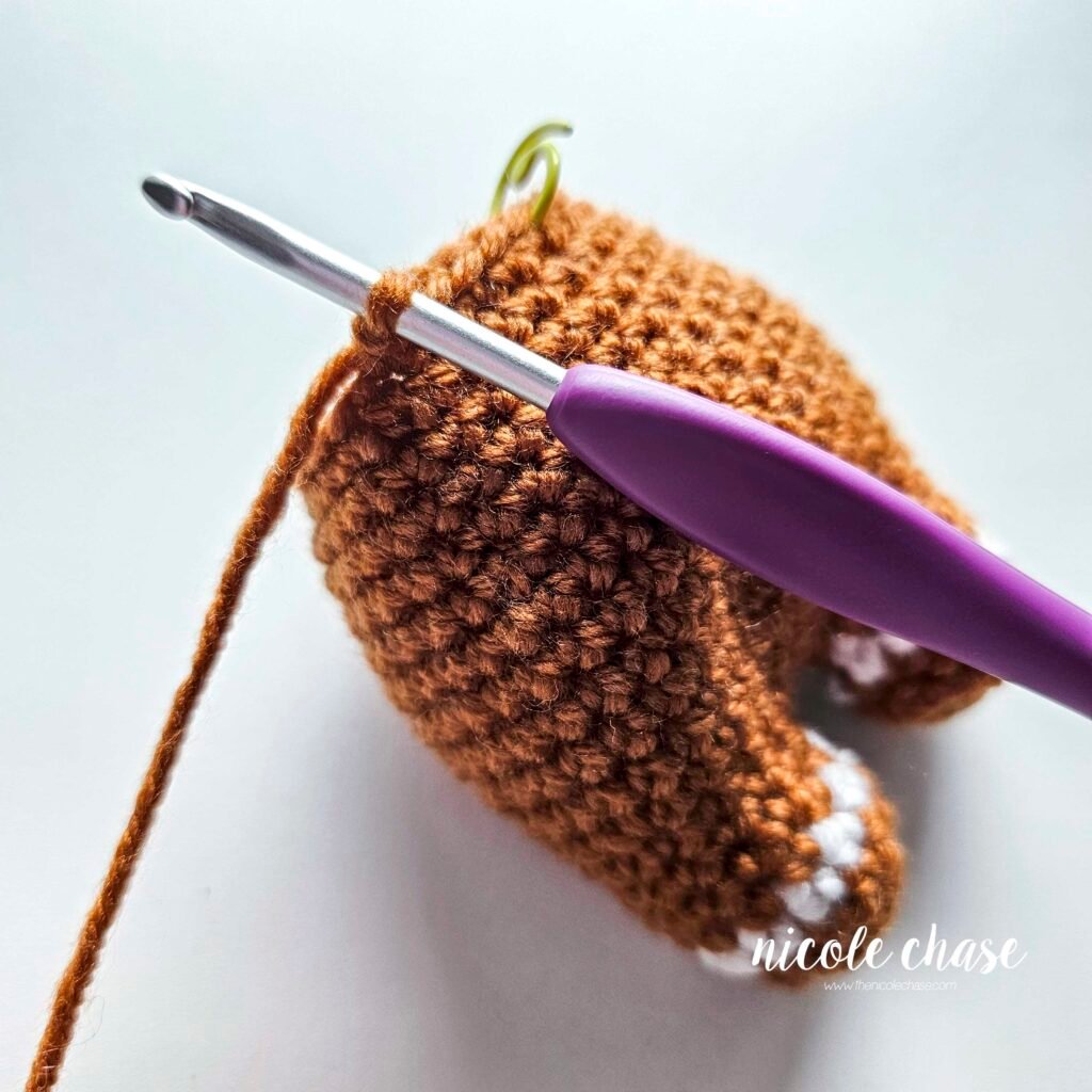 Tutorial photo showing the method for attaching the two crocheted arms at R20 of the nearly no-sew crochet gingerbread man pattern, step 1.