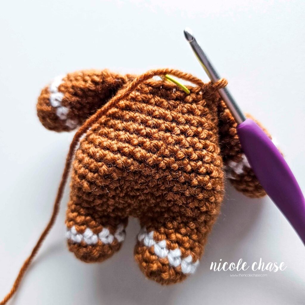 Tutorial photo showing the method for attaching the two crocheted arms at R20 of the nearly no-sew crochet gingerbread man pattern, step 9.