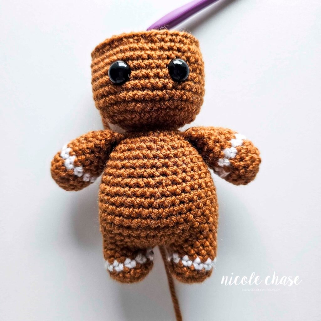 Showing the correct placement of the black safety eyes onto the crocheted head of the free crochet gingerbread man pattern. 