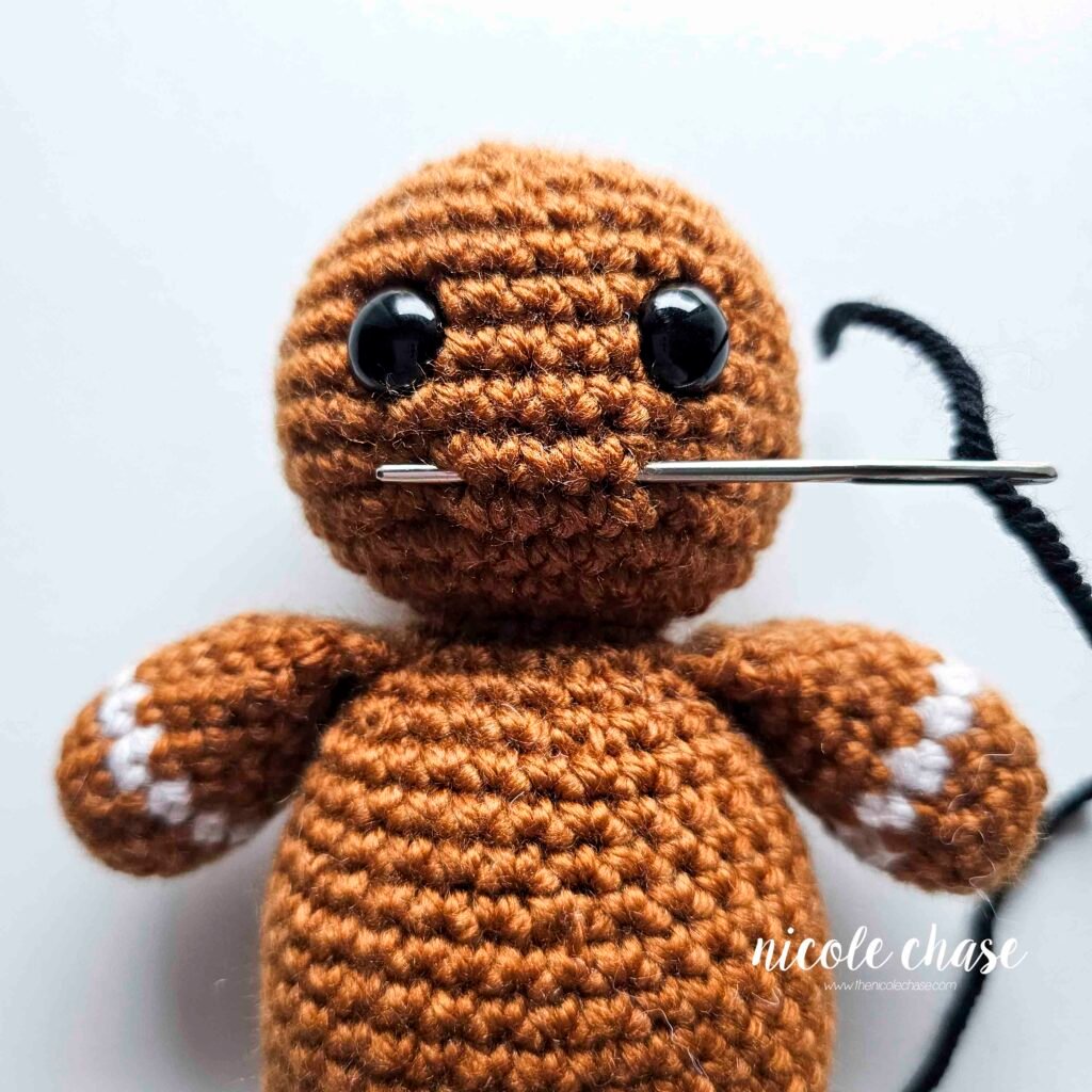 Embroidering a smile on the head of the free gingerbread crochet pattern, step 1.