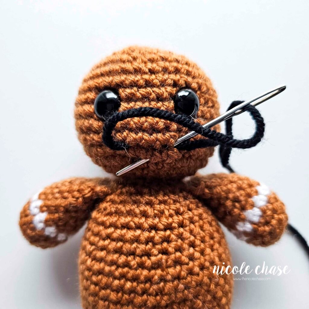 Embroidering a smile on the head of the free gingerbread crochet pattern, step 2.