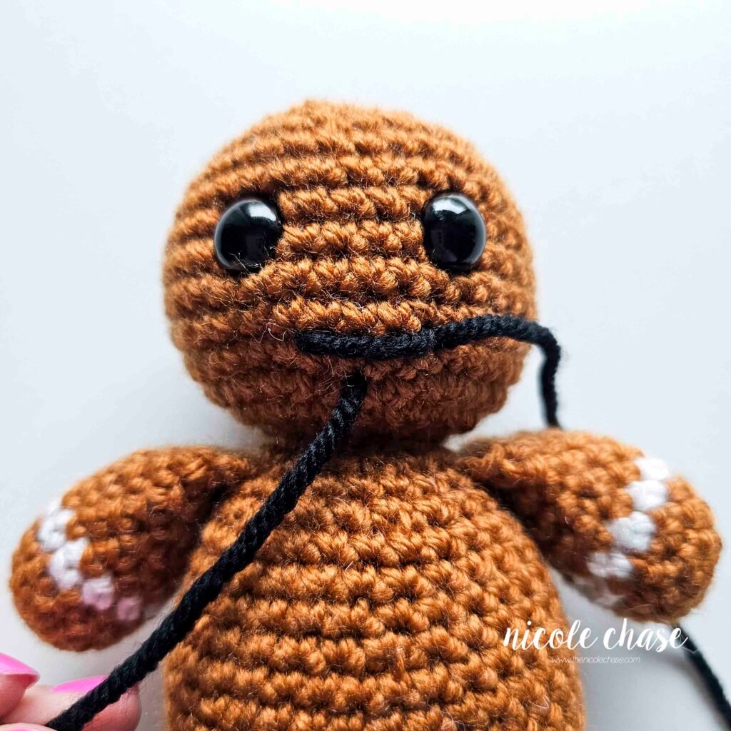 Embroidering a smile on the head of the free gingerbread crochet pattern, step 3.