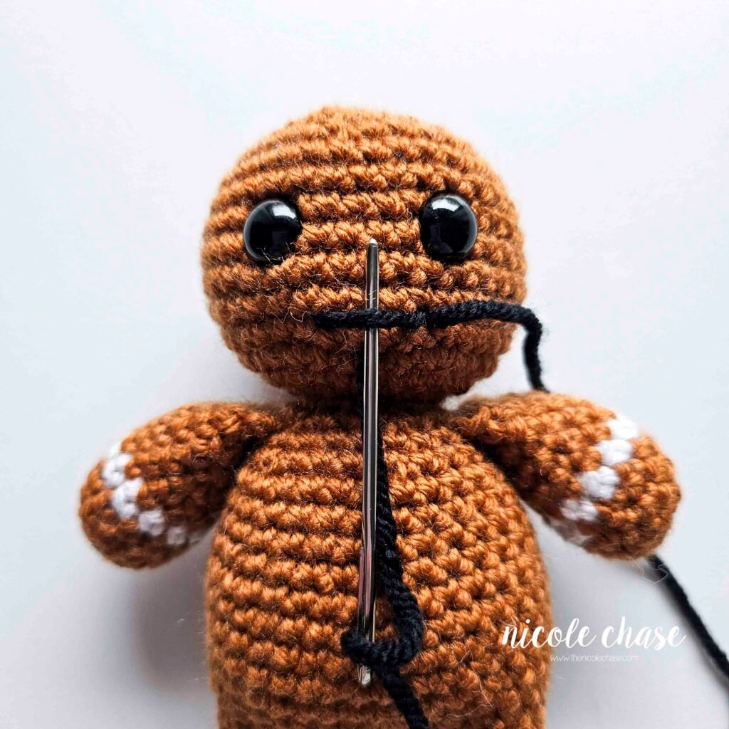 Embroidering a smile on the head of the free gingerbread crochet pattern, step 4.