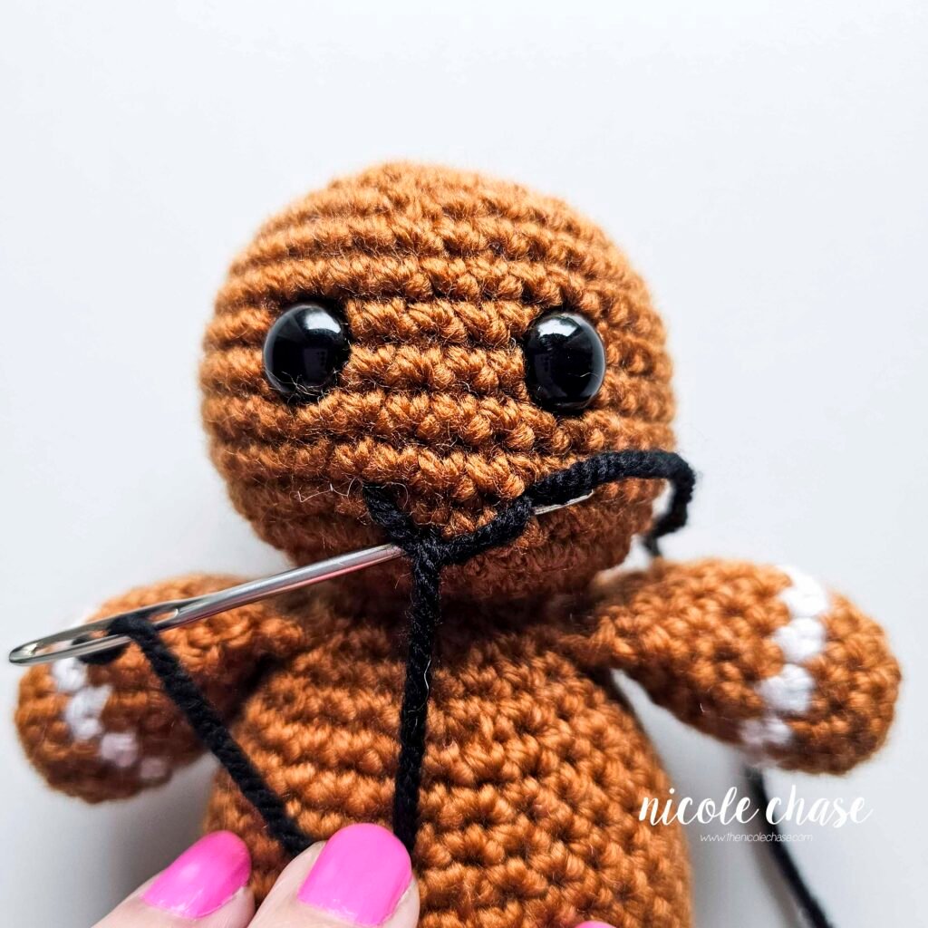 Embroidering a smile on the head of the free gingerbread crochet pattern, step 5.