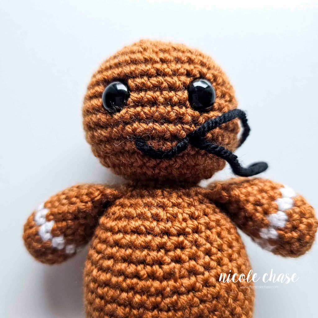 Embroidering a smile on the head of the free gingerbread crochet pattern, step 6.