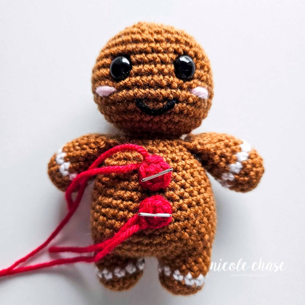 The buttons of the crochet gingerbread man have been pinned into place prior to sewing. 