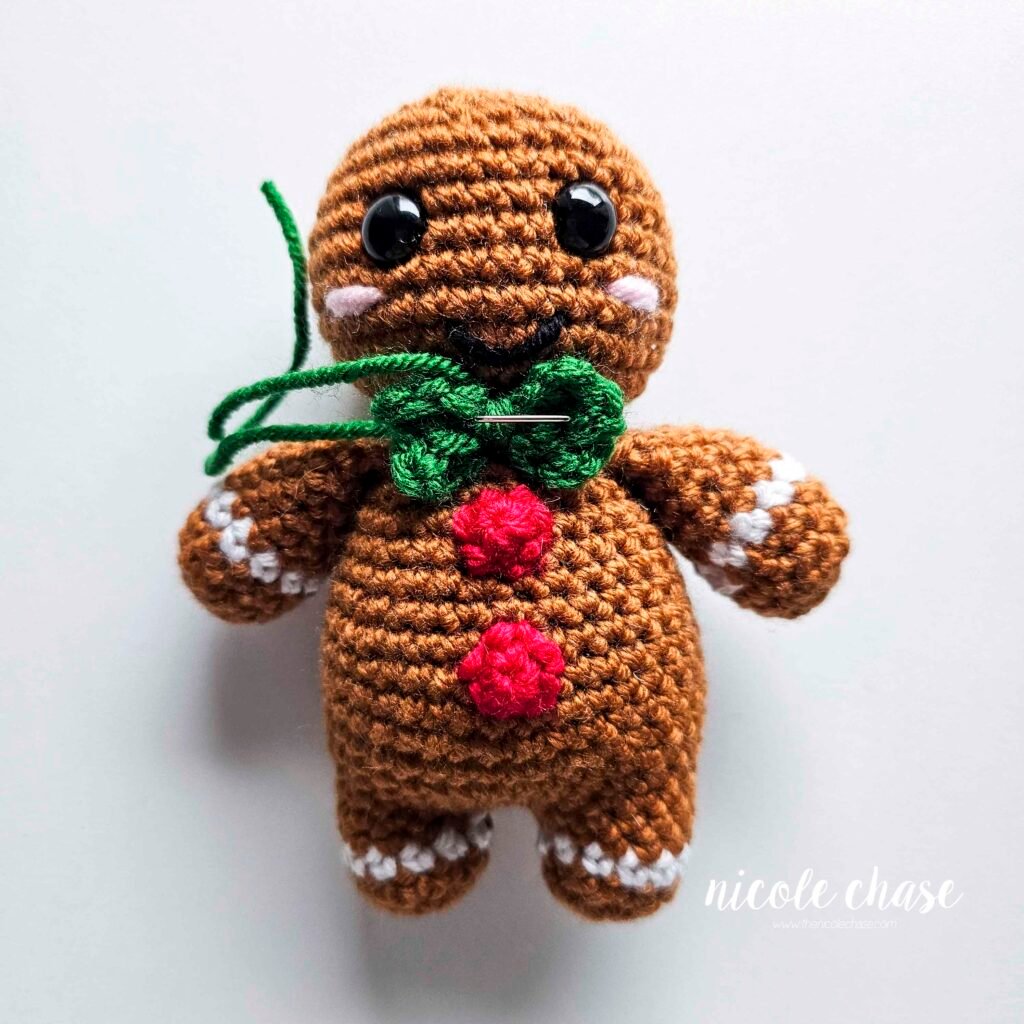 Tutorial image demonstrating the placement of the bow as a bow tie under the head of the crochet gingerbread man. 