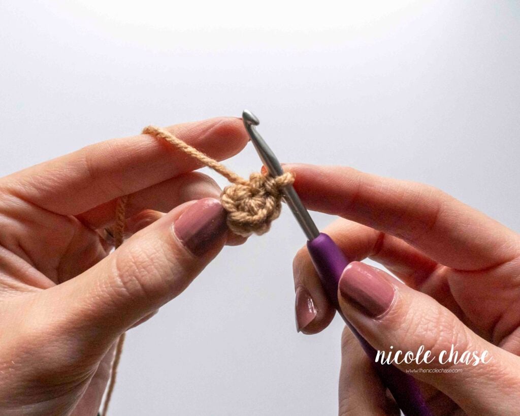 Close-up of a small, flat crochet piece after the completion of the first round, showing the smooth right side texture. "V" shapes are visible and facing you.
