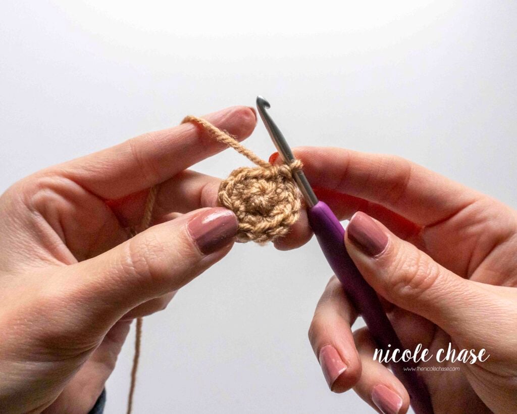 Close-up of a small, flat crochet piece after the completion of the second round, showing the smooth right side texture. "V" shapes are visible and facing you.