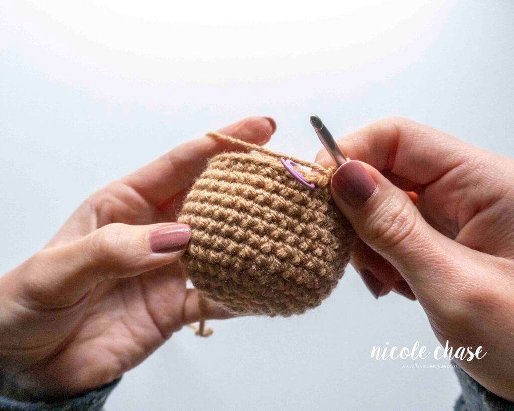 Views of a hand being able to comfortably crochet the decreasing round after the piece has been flipped to the smooth right side.