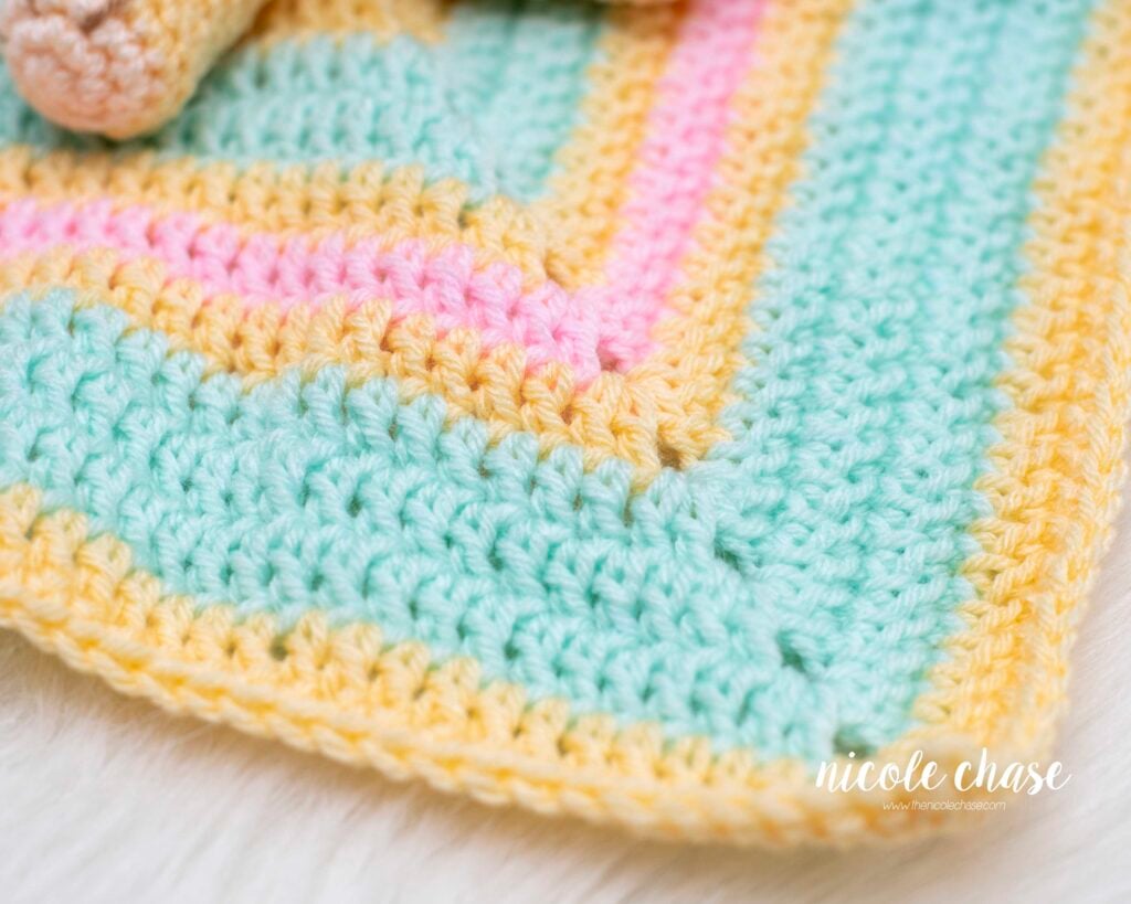 Close-up of the crochet blanket portion of the Hug Me Lion Lovey crochet pattern, showing pastel stripes of yellow, mint, and pink.