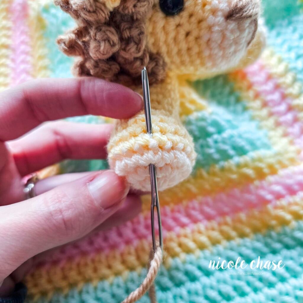 Embroidering nails on the arm of the crochet lion lovey, step 1.