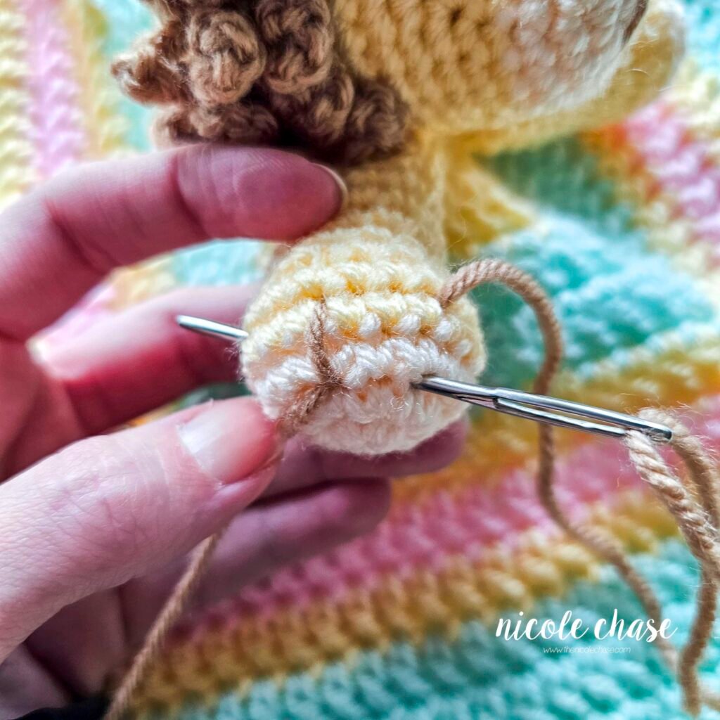 Embroidering nails on the arm of the crochet lion lovey, step 2.