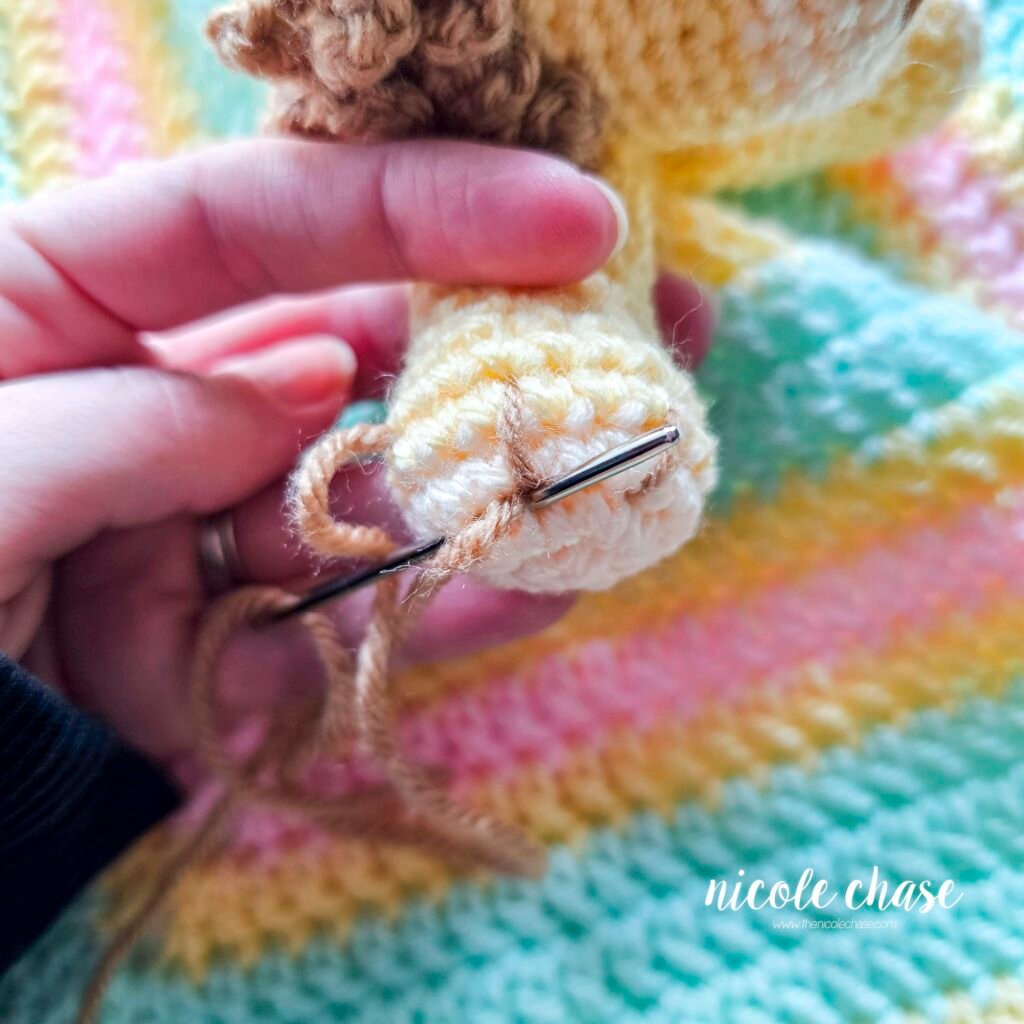 Embroidering nails on the arm of the crochet lion lovey, step 3.