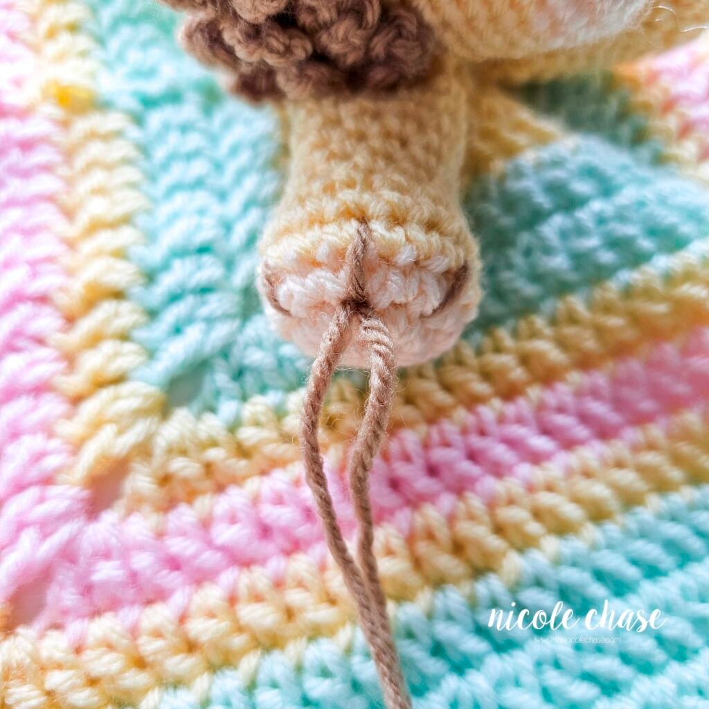 Embroidering nails on the arm of the crochet lion lovey, step 4.