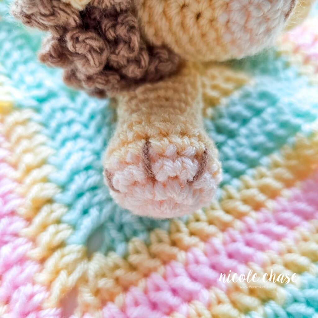 Embroidering nails on the arm of the crochet lion lovey, step 5.