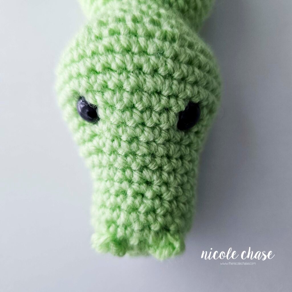 The nostrils of the crochet alligator have been sewn into place on the front of the head, view 2.