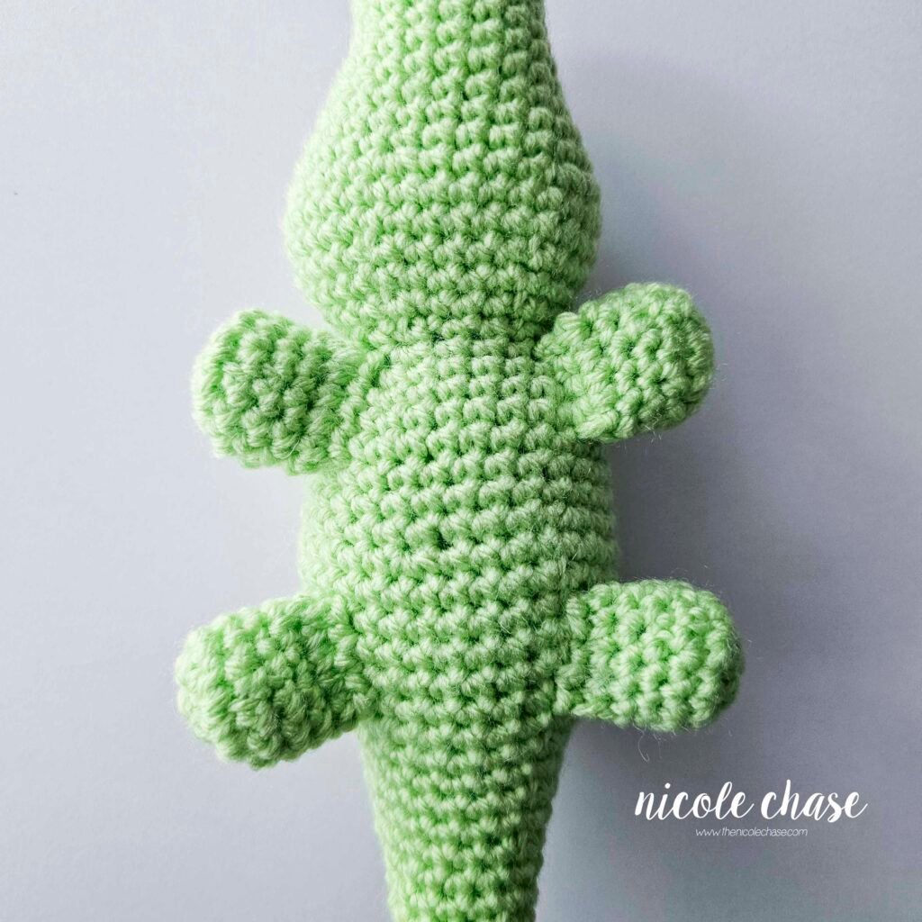 The legs of the amigurumi alligator have been sewn into place on the bottom sides of the crochet alligator pattern, view 1.