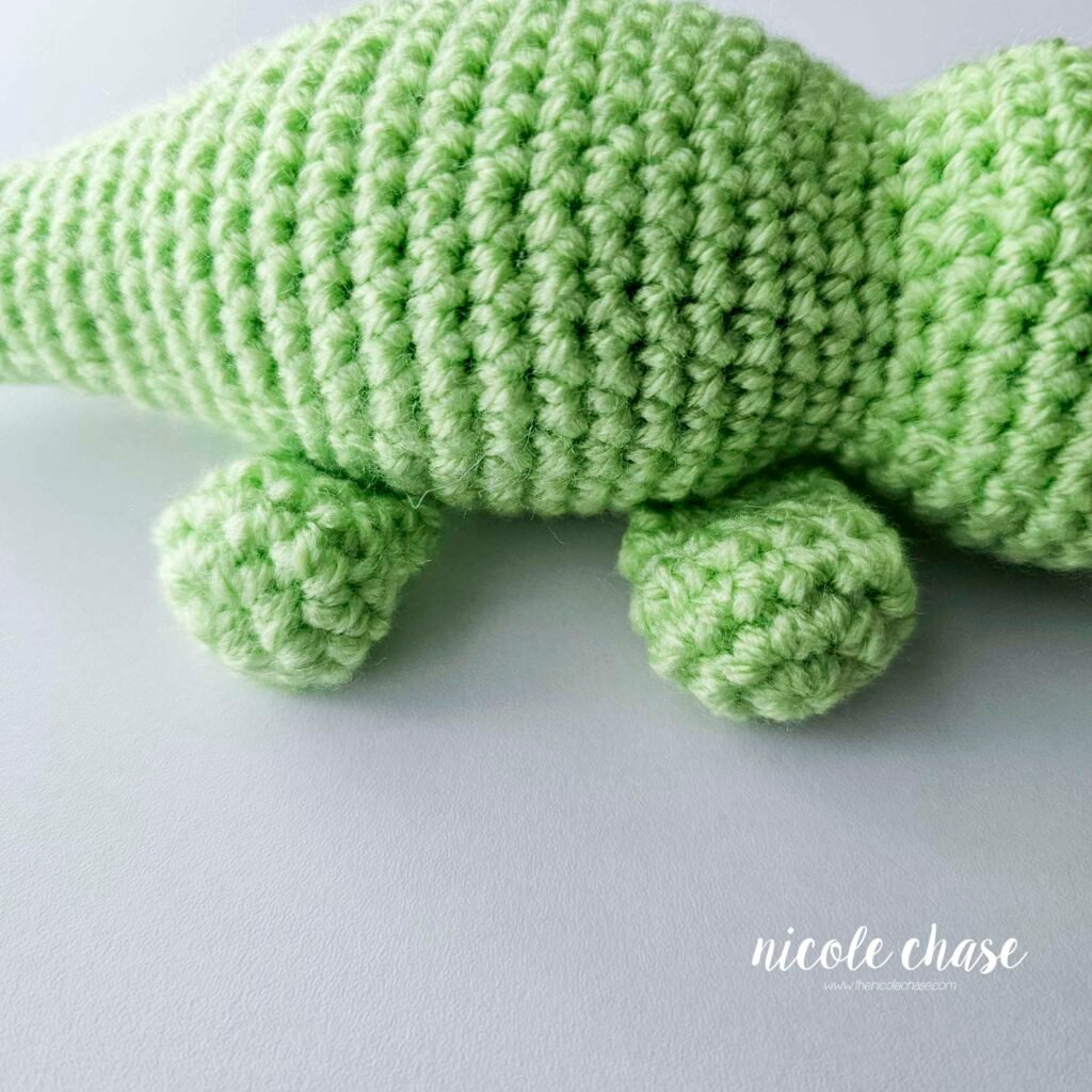 The legs of the amigurumi alligator have been sewn into place on the bottom sides of the crochet alligator pattern, view 2.