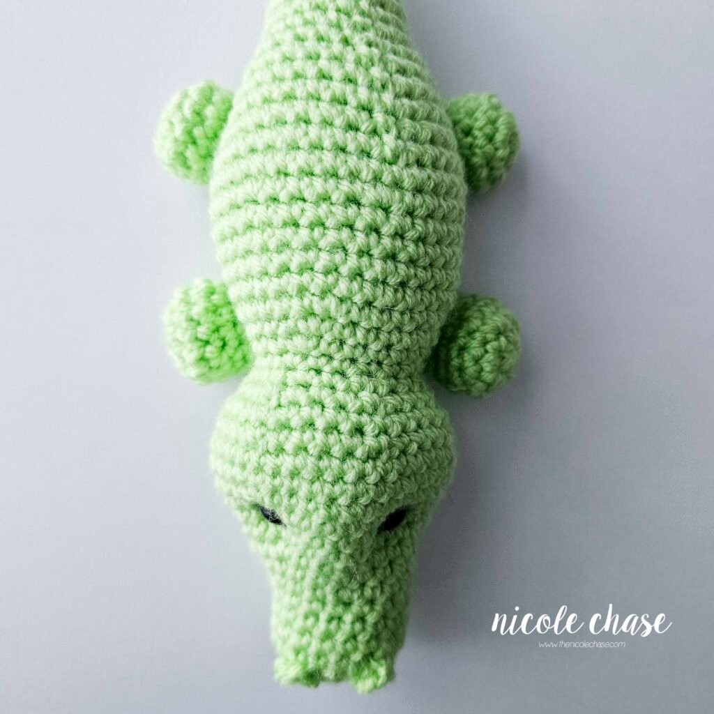 The legs of the amigurumi alligator have been sewn into place on the bottom sides of the crochet alligator pattern, view 3.