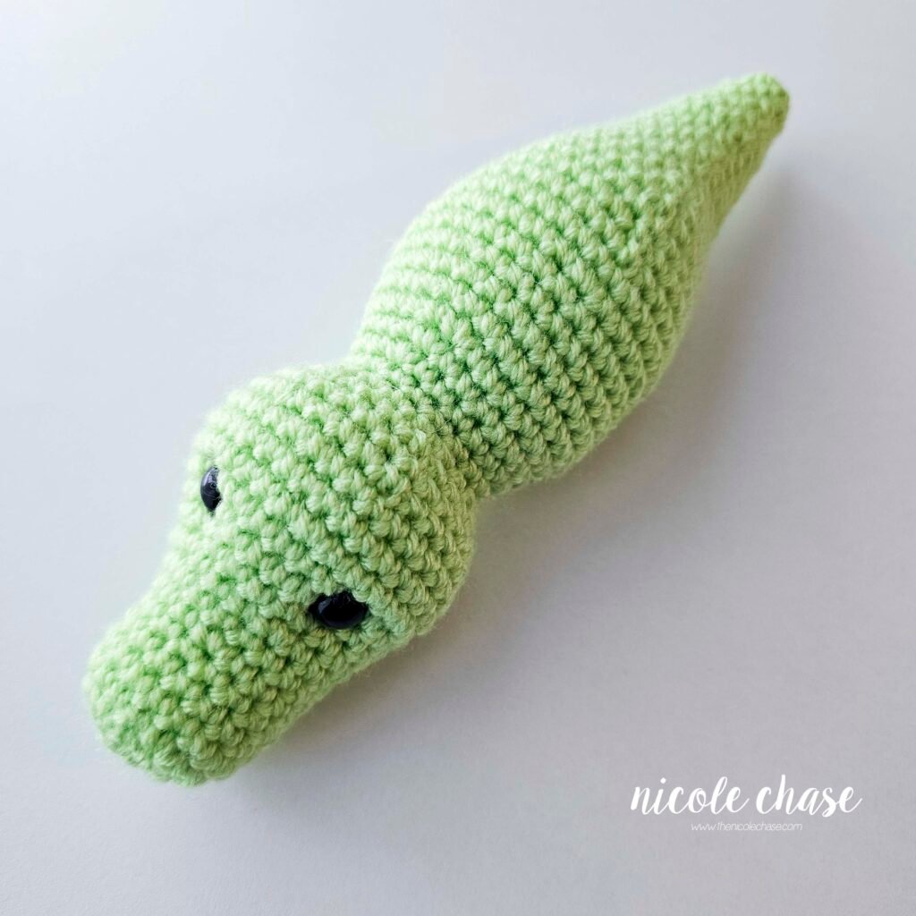 The finished head, body, and tail of the free alligator crochet pattern shown in a bright green yarn.