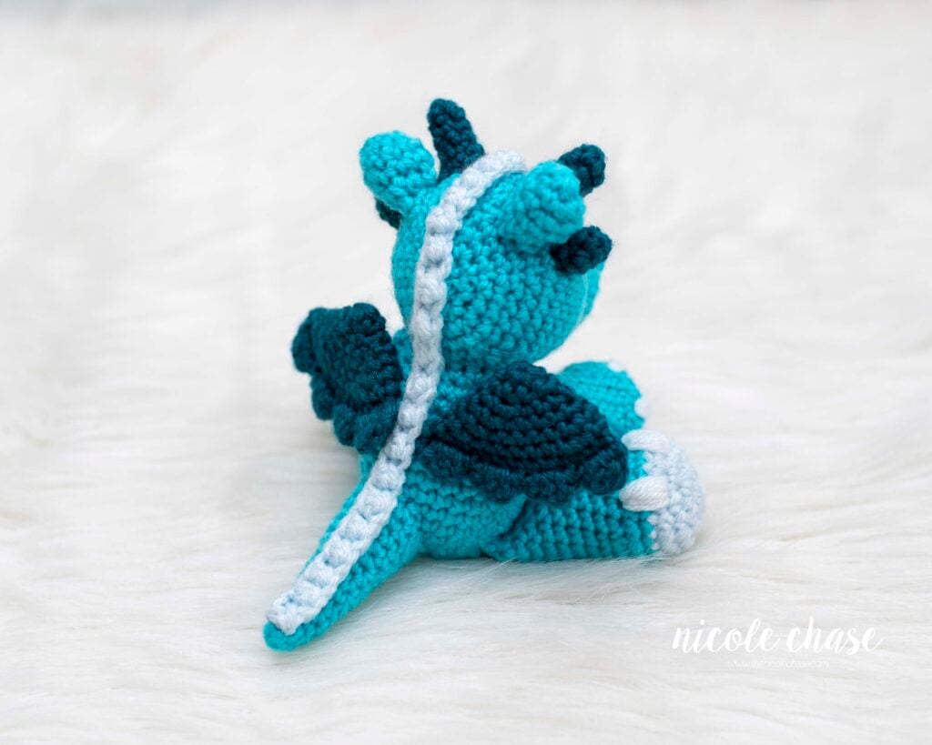 A view of the back of the dragon amigurumi to highlight the details of the light blue ridges down the back, and the dark teal wings on either side.