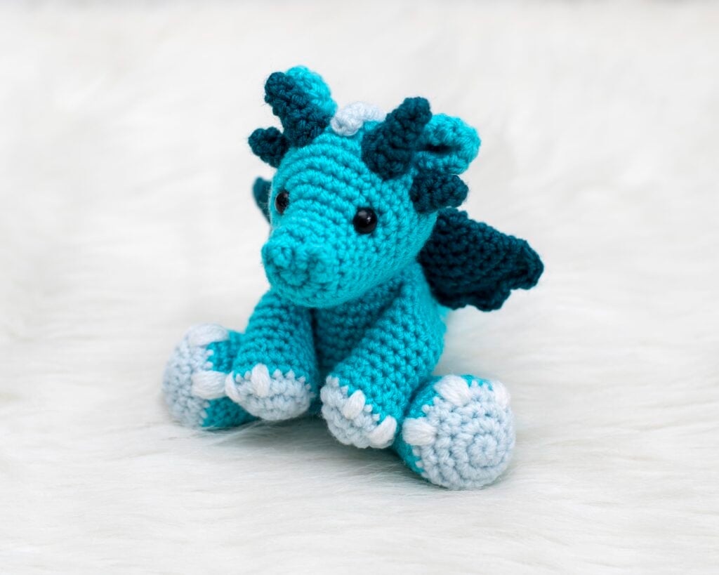 A blue amigurumi dragon with teal wings and horns and light blue details made from the free dragon crochet pattern designed by Nicole Chase.