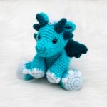 A blue amigurumi dragon with teal wings and horns and light blue details made from the free dragon crochet pattern designed by Nicole Chase.