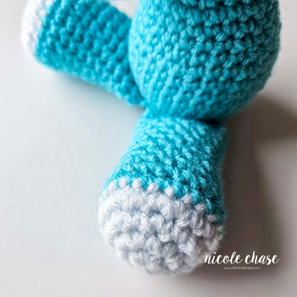 The crochet legs of the dragon have been sewn into place on the front of the body, and the legs are out in a sitting position.